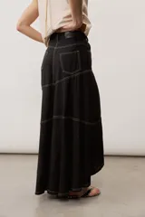 Falda larga de lino color beige, de corte asimétrico con costuras decorativas pespunteadas en contraste y diseño envolvente con bajo más largo en la parte trasera.