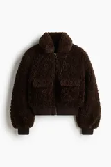 Campera corta de textura efecto peludito en color marrón oscuro. Presenta cuello alto, cierre frontal, bolsillos delanteros con solapa y puños y bajo en punto acanalado.
