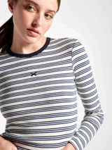 Camiseta de manga larga con cuello redondo, confeccionada en tejido acanalado con diseño de rayas horizontales en tonos claros y bordó. Presenta un pequeño bordado decorativo en el centro del pecho.