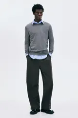 Buzo de punto fino color gris oscuro, de manga larga y cuello redondo, con remates acanalados en cuello, puños y bajo.