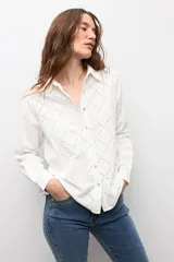 Camisa blanca de manga larga con frente de tela broderie con diseño de rombos calados y espalda lisa. Presenta cuello clásico y cierre frontal con botones.