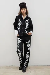 Camisa de denim negro con estampa floral blanca, cuello camisero, cierre frontal con botones y mangas largas.