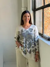 Sweater de punto con cuello en V y mangas largas, de diseño holgado. Presenta un estampado abstracto en tonos verdes con detalles metalizados en color dorado sobre una base de color crema.
