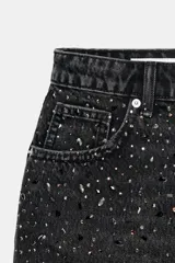 Shorts de denim negro de tiro alto con cinco bolsillos. Presenta aplicaciones de brillos plateados dispersos en la parte delantera y un bajo deshilachado.