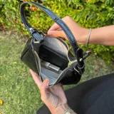 Cartera de hombro color marrón oscuro con textura de cocodrilo (efecto croco) y acabado brillante. Tiene forma de media luna y asa corta.