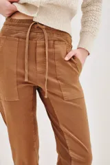 Pantalón tipo babucha de gabardina elastizada, color negro, con cintura elástica ajustable mediante cordón, puños en los tobillos, bolsillos diagonales frontales y bolsillos traseros con solapa y botón.