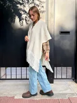 Ruana tejida de lana en color crudo, con diseño de flecos en los bordes. Es una prenda versátil y abrigada, ideal para complementar diversos looks.