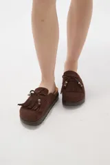 Suecos tipo mocasín color chocolate, confeccionados en material gamuzado. Presentan un diseño con flecos frontales, cordones decorativos con cuentas y una suela de plataforma plana de goma.