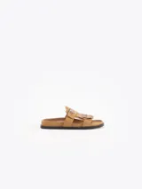 Sandalias planas color tostado de cuero vacuno, con capellada adornada con flecos y una tira con hebilla metálica.