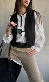 Chaleco negro de gamuza sintética, de estilo boho-chic, con costuras decorativas en los bordes y diseño clásico atemporal.