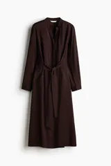 Vestido midi de manga larga en color marrón, con cuello mao abierto, cierre frontal con botones ocultos, puños abotonados y cinturón ajustable para anudar en la cintura.