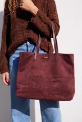 Bolso tipo tote de gran tamaño en color bordó, confeccionado en material con textura similar a la gamuza. Cuenta con doble asa larga para llevar al hombro y una pequeña placa metálica decorativa en el frente.