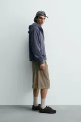 Bermuda wide fit color beige, confeccionada en pana de algodón. Presenta pliegues frontales en la cintura, bolsillos delanteros y bolsillos traseros de plastrón. Cierre frontal con cremallera y botón.