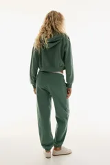 Pantalón de jogging verde con interior cepillado suave, cintura elástica fruncida con cordón ajustable, bolsillos laterales discretos y elástico revestido en los bajos.