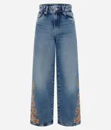 Pantalón wide leg de jean azul con bordado floral aplicado en los laterales. Posee cintura mediana con trabillas, cierre frontal con botón y cremallera, y bolsillos funcionales.