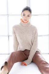 Sweater de punto color beige con cuello alto y ribete naranja en cuello y puños.
