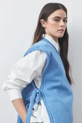 Chaleco tejido de punto con silueta relajada y diseño sin mangas. Presenta lazos laterales ajustables y cuello redondo.