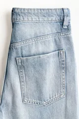 Jean de tiro alto con pierna amplia y corte holgado, confeccionado en denim rígido de tono azul claro con efecto desgastado. Presenta diseño clásico de cinco bolsillos, cierre frontal con botón y costuras reforzadas.