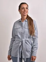 Camisa color beige con cuello clásico, cierre frontal con botones, dos bolsillos con solapa en el pecho y mangas largas con puños abotonados.