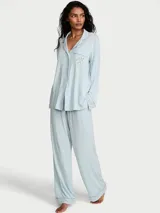 Pijama largo de modal color celeste, compuesto por una camisa de manga larga con cuello solapa, botones frontales y bolsillo en el pecho con aplique de corazón de margarita, y pantalón largo de corte recto con cintura elástica.