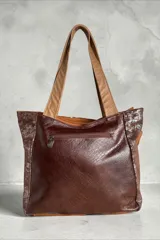 Cartera tipo shopper confeccionada en cuero con diseño patchwork en tonos marrones y animal print, asas de hombro en tono tostado y detalle de dije colgante metálico triangular.