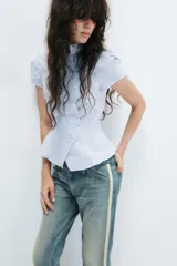 Camisa de manga corta con estampado de rayas verticales en tonos celeste y blanco, cuello alto y cierre frontal cruzado con botones.
