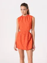 Vestido corto color naranja con textura floral en relieve, cuello alto, corte a la cintura y falda balloon. Presenta aberturas laterales.