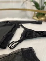 Conjunto de lencería compuesto por un top de cuello alto con mangas largas de microtul y detalles de encaje, y una tanga regulable de terciopelo y encaje.