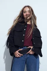 Campera negra de estilo western con flecos en las mangas, corte cropped, bolsillos frontales y cierre con botones metálicos.