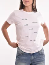 Remera blanca de manga corta con estampado frontal que dice "hecha pa brillar" en tonos rosados y estrellas.