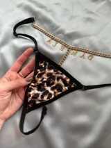 Tanga tipo colaless con estampado animal print de leopardo, tiras ajustables negras y detalle de cadena dorada con dijes de letras.