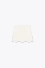 Falda pantalón corta de tiro alto color blanco con bordados florales perforados y forro interior. Cierre lateral con cremallera oculta.