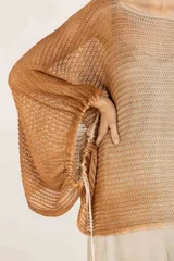 Poncho amplio de punto calado en mezcla de algodón y acrílico, con mangas regulables con jareta, degradé hecho a mano con aerógrafo, escote redondo, silueta oversize y largo a la cadera.