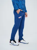 Pantalón de entrenamiento Umbro del Club Nacional de Football, modelo Grok en color azul. Presenta el escudo del club en una pierna y el logo de Umbro en la otra, con diseño cómodo y deportivo.