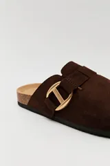 Zueco de estilo casual con capellada cerrada en material tipo gamuza color negro. Presenta una hebilla metálica decorativa en tono dorado sobre el empeine y una base anatómica con efecto corcho.