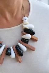 Collar de diseño artesanal compuesto por piezas de resina en forma de gotas y cilindros alargados en tonos blanco, negro y marrón, montadas sobre un cordón de hilo encerado.
