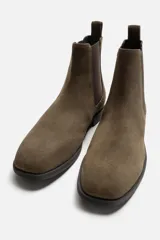 Bota estilo Chelsea de piel con acabado serraje color beige, con elásticos laterales para facilitar el calce, horma redonda y suela a tono con ligero tacón.