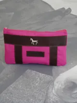 Sobre o cartuchera de lona fucsia con terminaciones y detalles de cuero marrón. Cuenta con cierre superior y aplique metálico de caballo en la parte frontal, además de una etiqueta de cuero con la marca grabada.