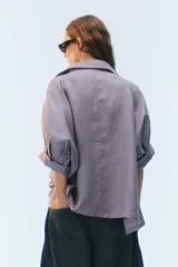 Camisa oversize blanca de lino, con corte cuadrado, mangas raglán cortas con puños anchos, aberturas laterales y cierre frontal de botones.