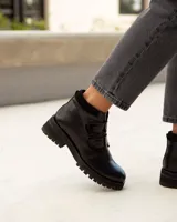 Bota corta de cuero color negro, estilo botín, con suela track gruesa y dos tiras ajustables con hebillas brillantes en el empeine.