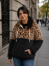 Buzo tipo canguro de tejido polar, con diseño combinado en animal print de leopardo en la parte superior y color negro en la parte inferior. Presenta capucha con cordones ajustables, cierre frontal parcial y bolsillo tipo canguro.