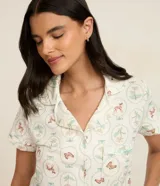 Conjunto de pijama de dos piezas, compuesto por una blusa de manga corta con cuello solapa, cierre frontal de botones y bolsillo en el pecho, y un short con cintura elástica y lazo de satén. El tejido es viscolycra con estampado de motivos florales y mariposas en círculos.