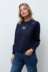 Blusa blanca de manga larga con cuello redondo, confeccionada en tela liviana con detalles de encaje vertical y bordado floral en el pecho.