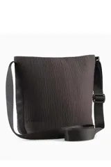 Cartera bandolera Puma tipo bucket bag, de color negro con diseño fruncido, correa ajustable y logo de la marca impreso en dorado en el frente.