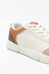 Zapatilla urbana blanca de mujer, con silueta moderna y líneas limpias. Presenta detalles en poliuretano liso y un panel plateado en el talón. La suela es de perfil recto y firme.