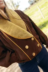 Chaqueta confeccionada en gamuza color negro con amplio cuello smoking de corderito en tono crudo. Presenta un diseño corto, cruzado con doble abotonadura y botones metálicos, mangas amplias y bolsillos.