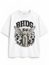 Remera blanca de algodón pesado con corte boxy, cuello redondo y mangas cortas. Presenta un estampado frontal en tonos gris y negro con la inscripción "BHDG" y la figura de un ángel rodeado de estrellas y fondo nebuloso.