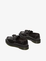 Mocasín Dr. Martens modelo Adrian, color bordó brillante, con borlas y costuras visibles. Confeccionado en cuero Arcadia, con empalmillado Goodyear y suela con cámara de aire resistente.