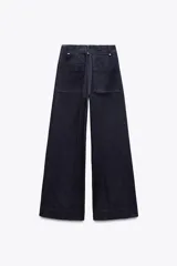 Jeans de tiro alto y pierna ancha de Zara, confeccionados en mezcla de algodón color beige. Presentan cintura con trabillas, bolsillos de parche en la espalda, costuras frontales marcadas y cierre delantero con cremallera, botón y gancho metálico.