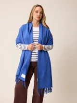 Pashmina de textura suave y color crema, con diseño liso y terminaciones en flecos en los extremos. Incluye una etiqueta decorativa en una de las esquinas.